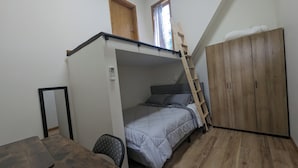 Habitación pequeña con literas, una escalera de madera, un armario y una mesita.