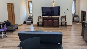 Una sala de estar moderna con un televisor de pantalla plana grande montado en la pared, un sofá de color oscuro y una mesa de comedor de madera con sillas.