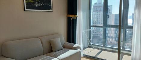 A modern living room with a beige sofa, a marble coffee table, and a large window offering a city view.