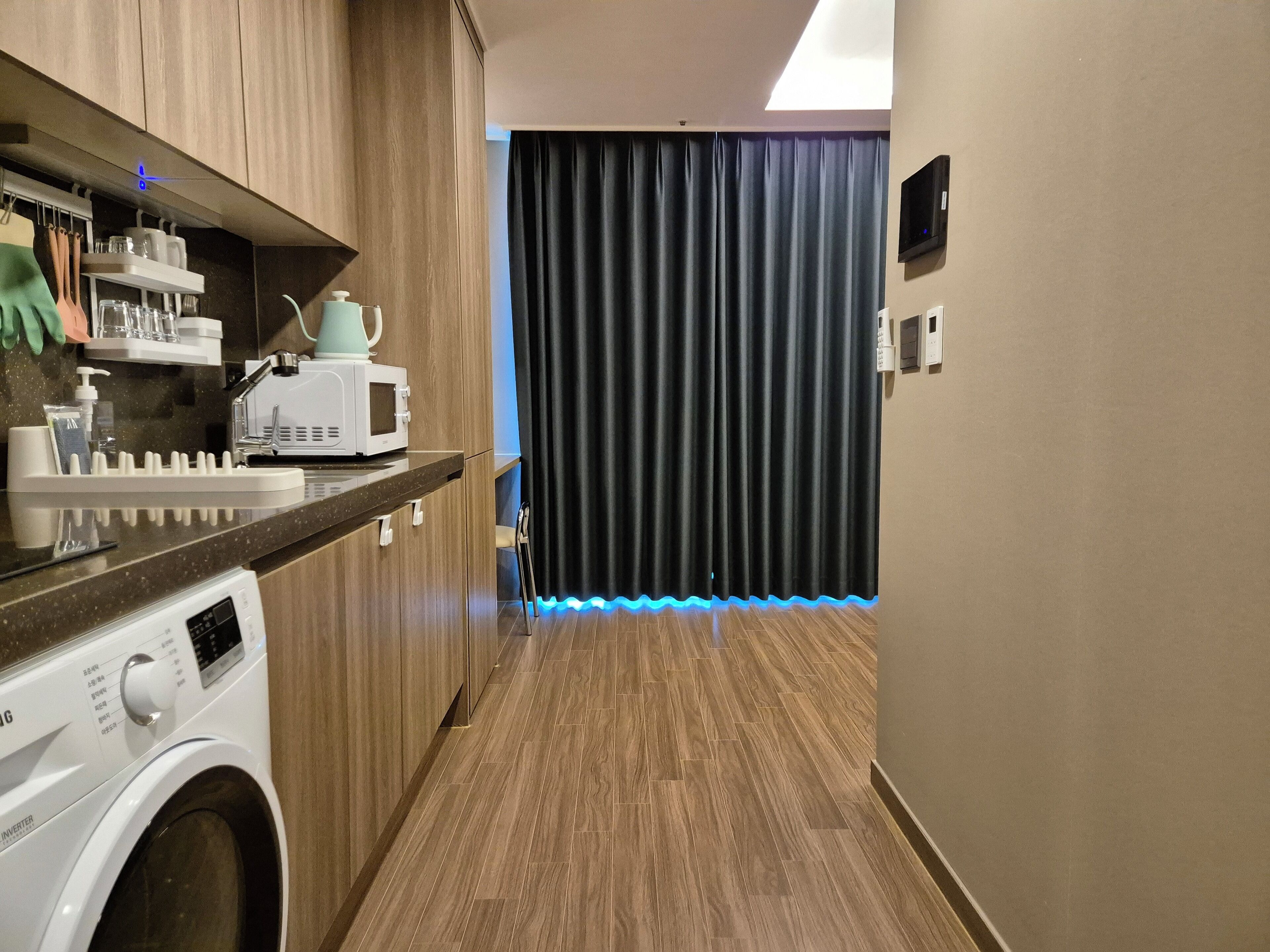 Een praktische keuken met een wasmachine, magnetron en een plank met keukengerei.