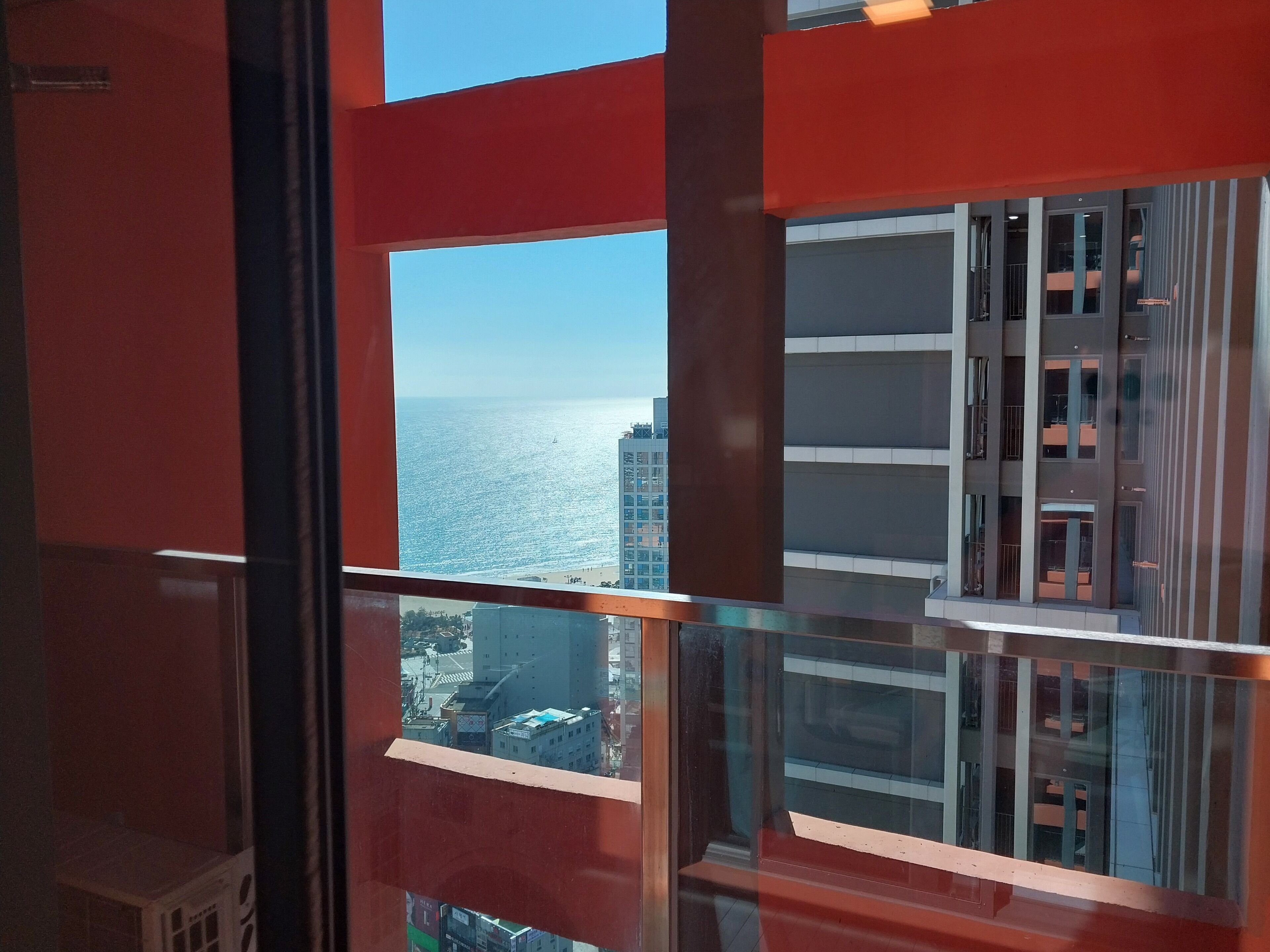 A view from a window with a red frame, overlooking a cityscape and a body of water.