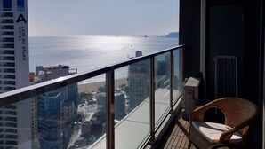 A balcony with a view of the sea and cityscape, a wicker chair, and a glass railing. - The solid residence - Elbon by haeundae (Busan)