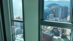 A view from a high-rise window overlooking a coastal cityscape with modern buildings and a beach. - The solid residence - Elbon by haeundae (Busan)