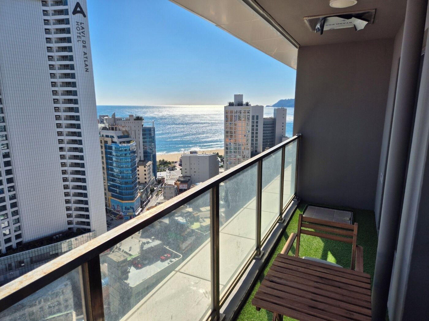 A balcony with a view of the beach and cityscape, including a tall building with 'LAVIE DE ATLANT HOTEL' signage.