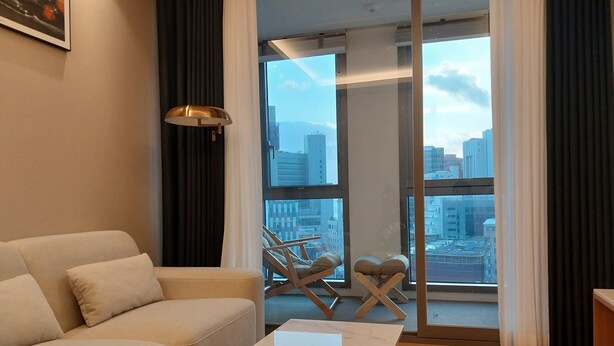 A modern living room with a sofa, a coffee table, and a view of the city through large windows. - The solid residence - Elbon by haeundae (Busan)