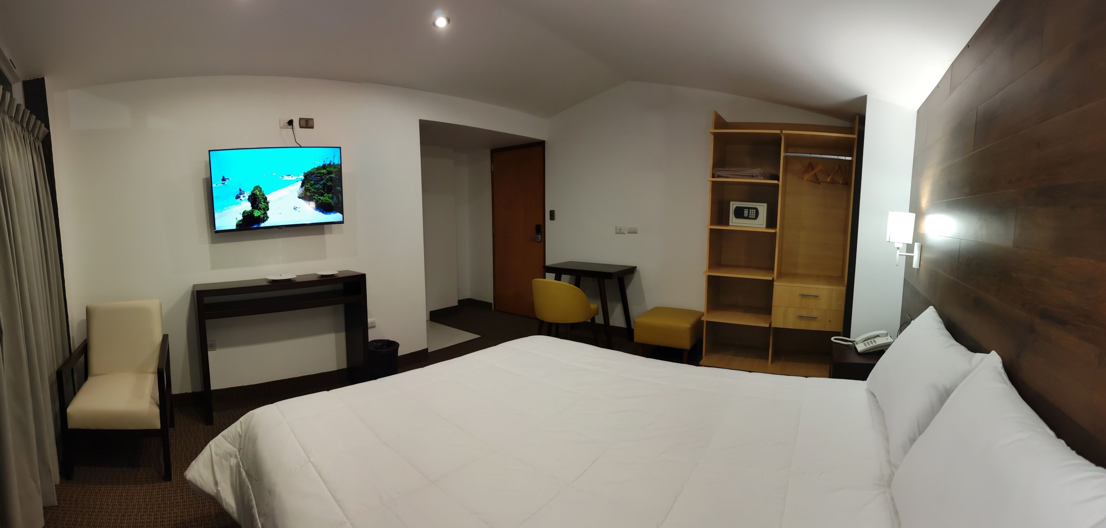 Habitación de hotel con una cama grande, un escritorio con silla, televisión, armario y una mesita.
