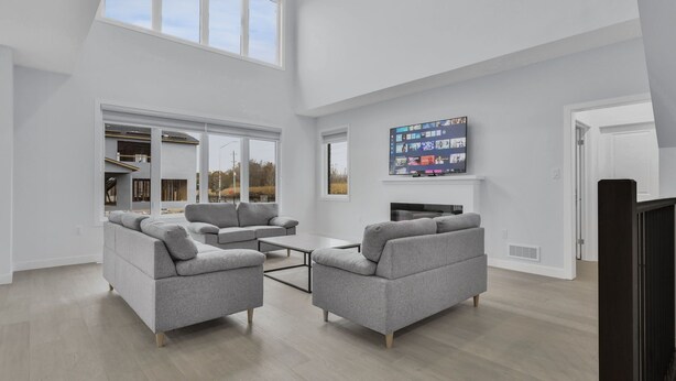 A spacious living room with a large TV, grey sofas, and a fireplace.
