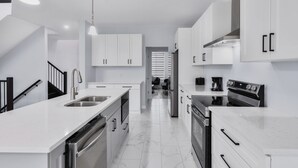 A modern kitchen with white cabinetry, stainless steel appliances, and a marble floor.