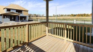 A covered outdoor deck with a view of a two-story house and a cornfield.