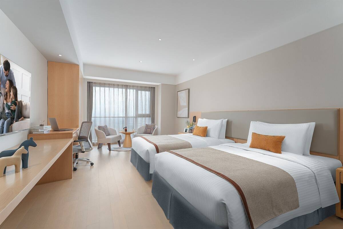 Habitación de hotel con dos camas, un escritorio, una silla y una mesita.