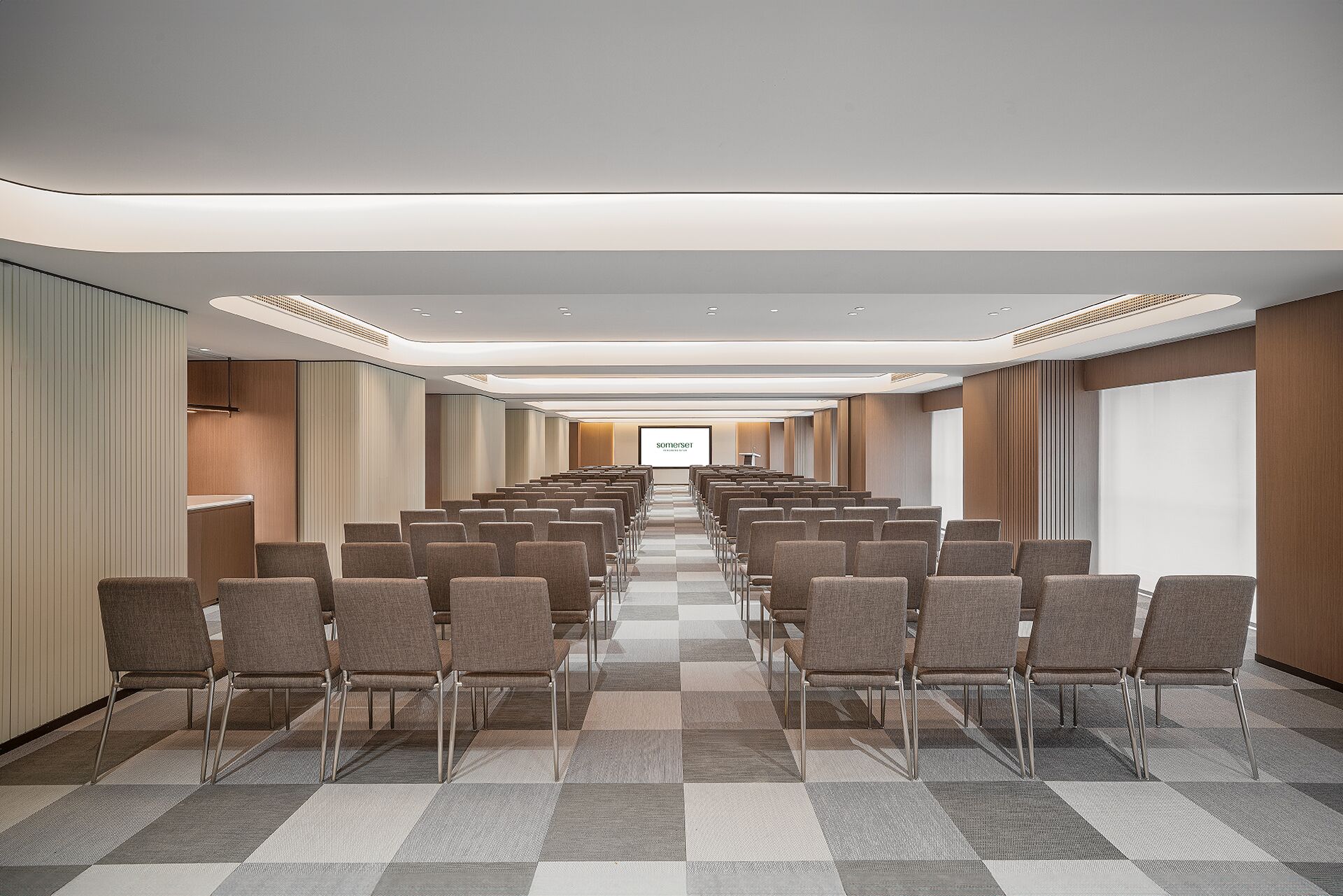 Une salle de conférence avec des rangées de chaises, un écran de projection et un espace dédié aux présentations à l’avant.