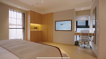A modern hotel room with a large bed, a desk with a computer, and a window with curtains.