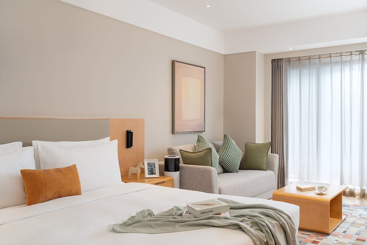 Una habitación de hotel con una cama grande, un sofá, una mesita y una ventana con cortinas.