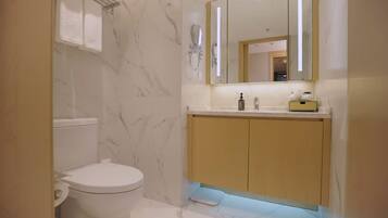 A bathroom with a toilet, marble walls, a sink with a mirror, and a cabinet.