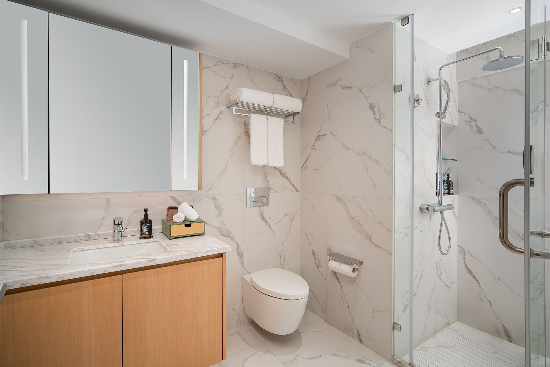 A modern bathroom with a marble floor, a glass shower enclosure, a toilet, and a vanity with a mirror and towel rack.