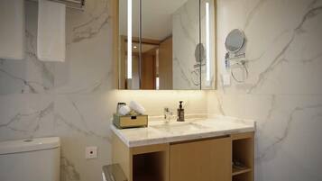 A bathroom with a marble countertop, a large mirror, a towel rack, and a toilet.