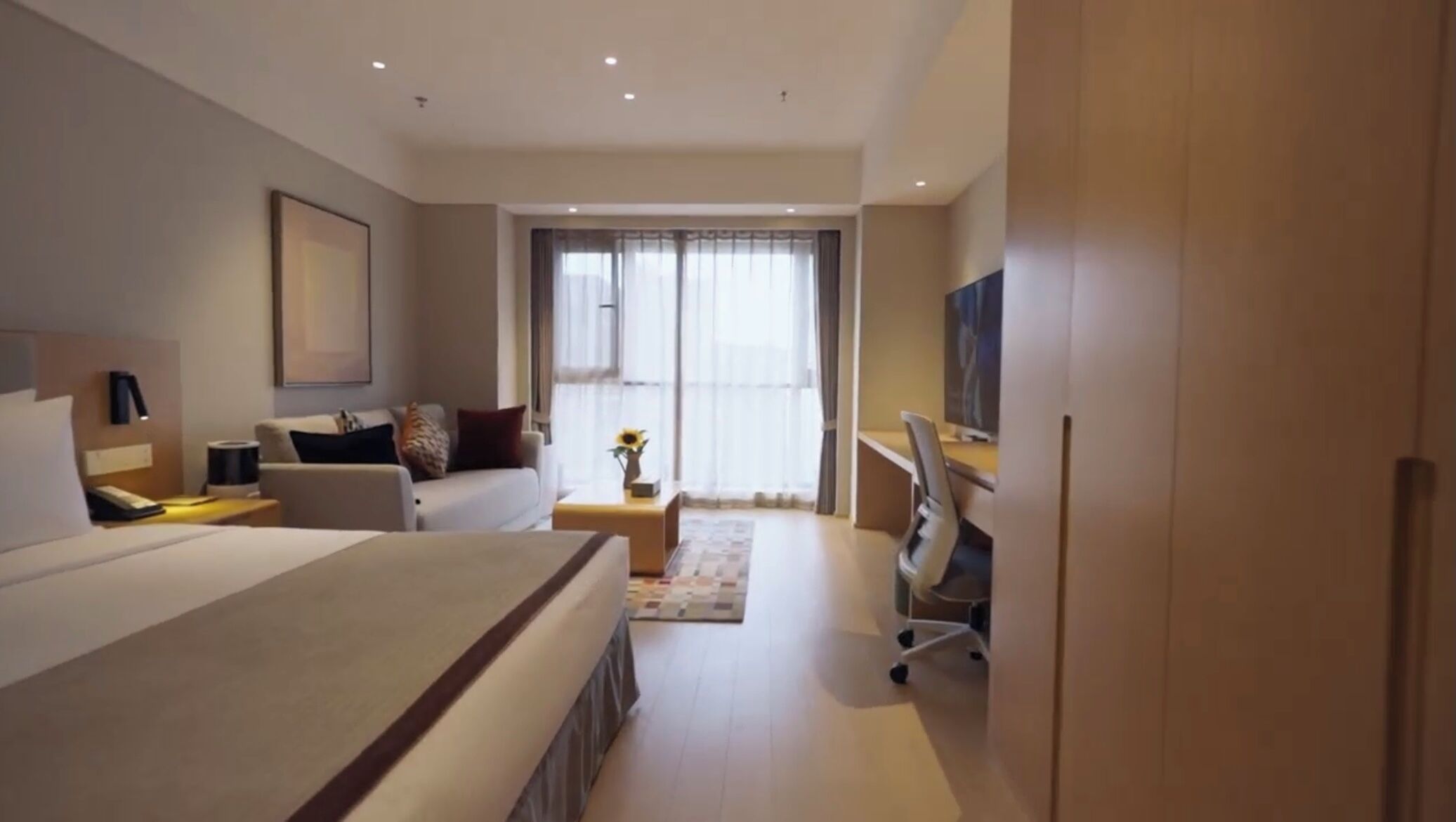 Une chambre d’hôtel moderne équipée d’un grand lit, d’un bureau, d’une chaise, d’une télévision et d’une fenêtre avec des rideaux.