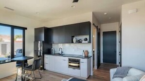 A modern kitchen with dark cabinets, a built-in oven, and a dining area with a table and chairs. - Zion Modern Lux Casita (Virgin)