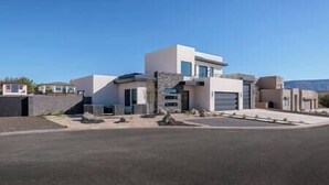 A modern two-story house with a garage, a stone facade, and a clear blue sky. - Zion Modern Lux Casita (Virgin)