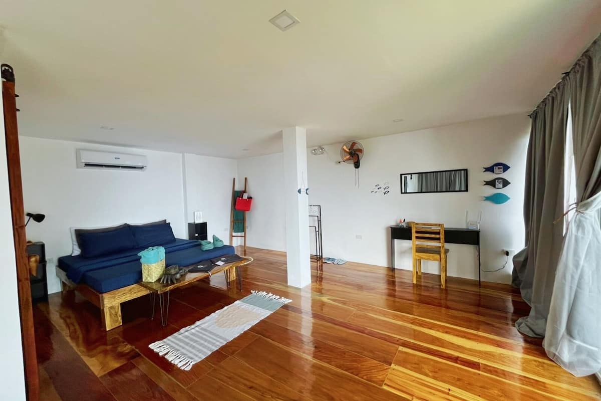 Ein modernes Wohnzimmer mit Holzboden, einem blauen Sofa, einem kleinen Tisch und einem Schreibtisch mit Stuhl.