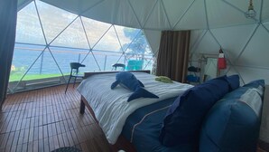 Une chambre d’hébergement sous tente, équipée d’un lit, d’oreillers et offrant une vue sur l’extérieur.