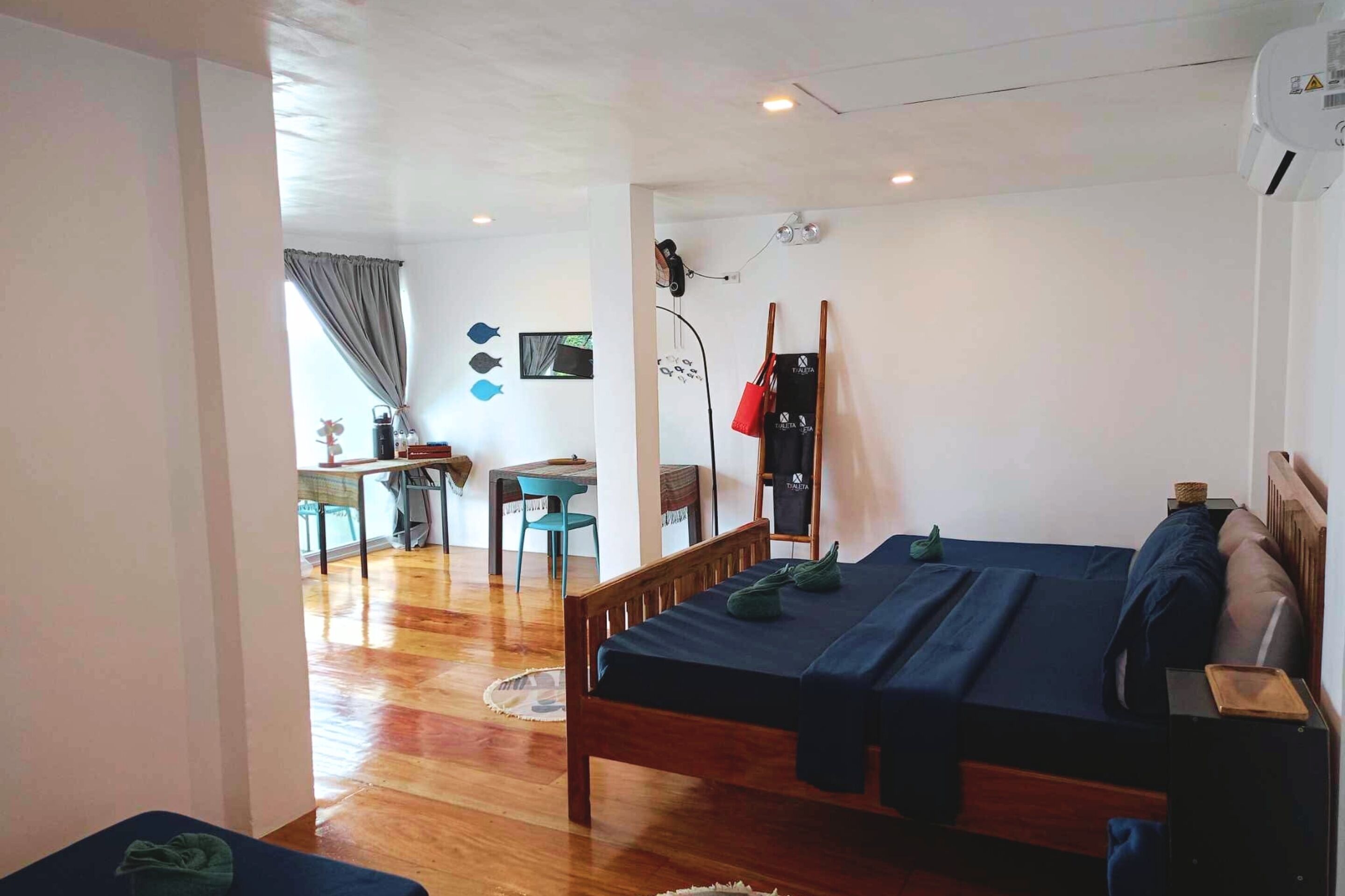 A room with a wooden bed, a desk with a chair, a small table, and a window with curtains.