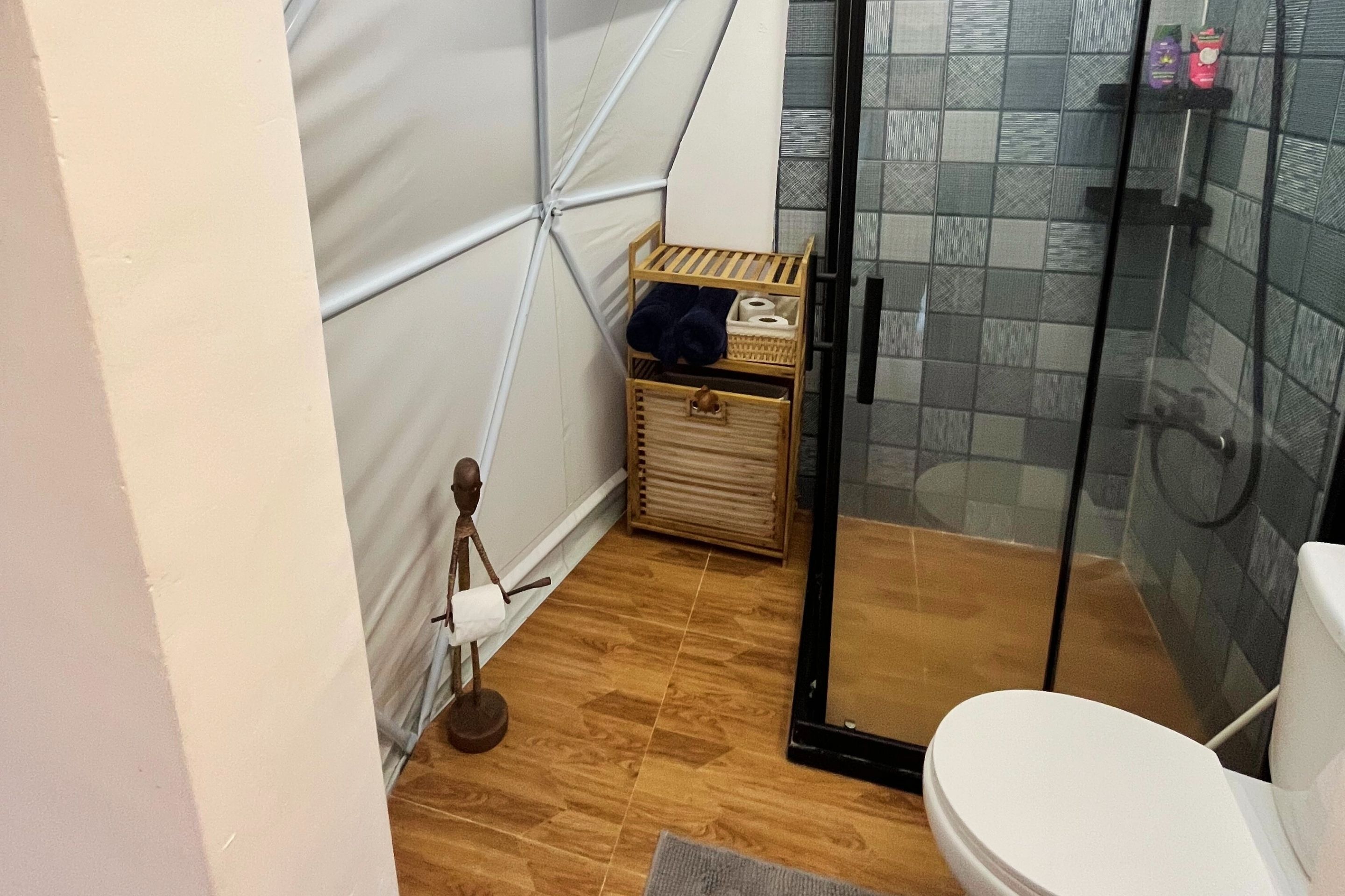Ein Badezimmer mit Duschkabine aus Glas, einer weißen Toilette und einer Holzkiste mit Handtüchern und Toilettenartikeln.