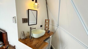 Une petite salle de bain avec un meuble-lavabo en bois, un lavabo blanc, un miroir et une petite statue de Bouddha.