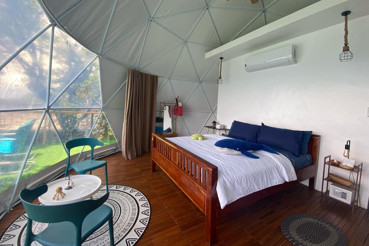 Ein Zelttraum mit Bett, Stuhl, kleinem Tisch und einer Hängeleuchte.