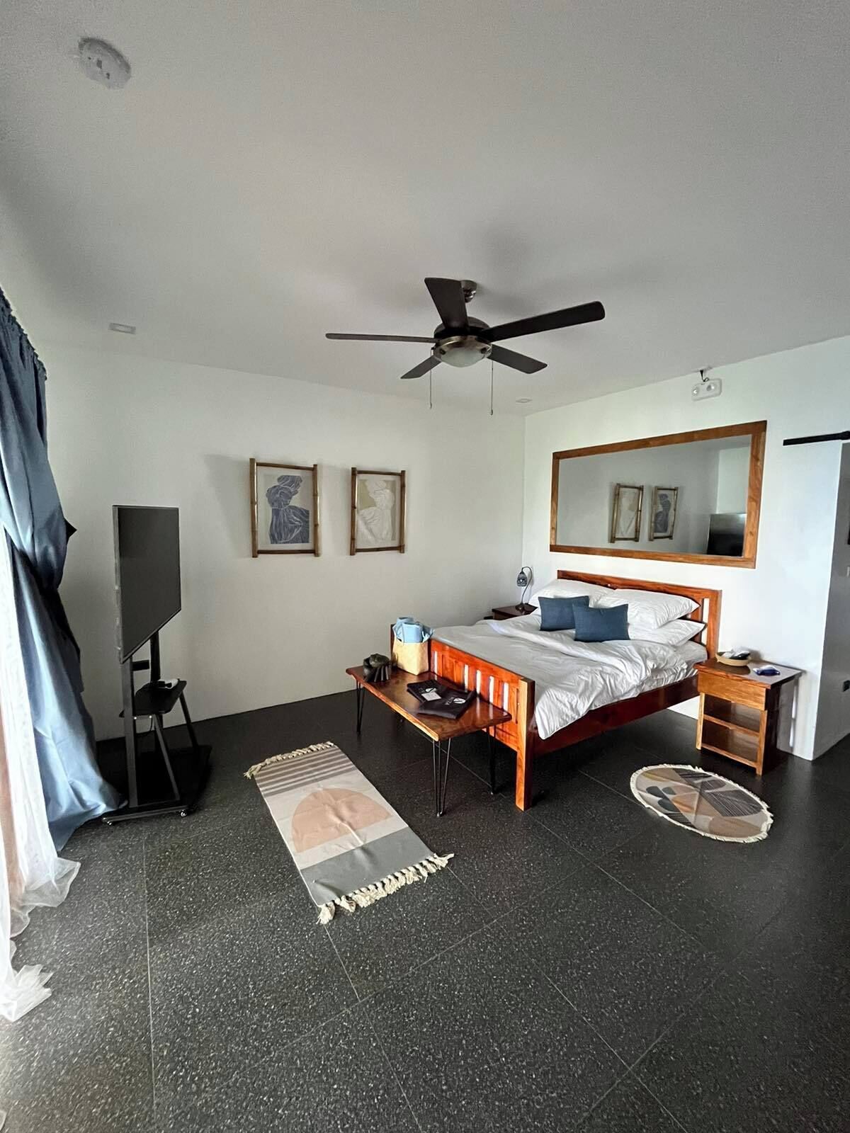 Une chambre à coucher comprenant un lit, un ventilateur de plafond, une table de chevet, un miroir et un meuble pour la télévision.