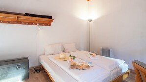 Una cama bien tendida con sábanas blancas, un sombrero, un libro y una rosa sobre la cama.