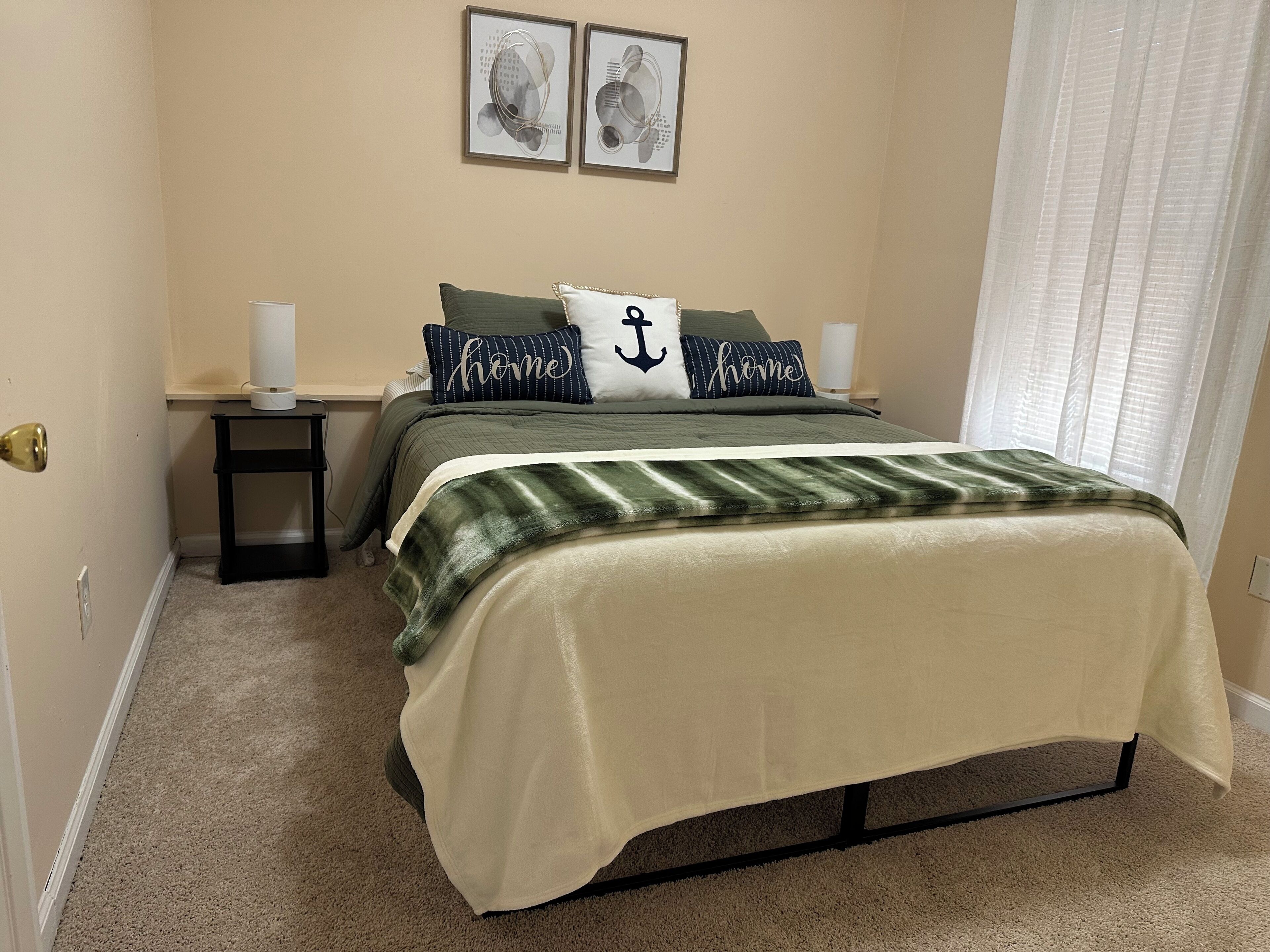 Une chambre à coucher comprenant un lit, deux tables de chevet, une commode, une fenêtre avec des rideaux et deux tableaux encadrés accrochés au mur.