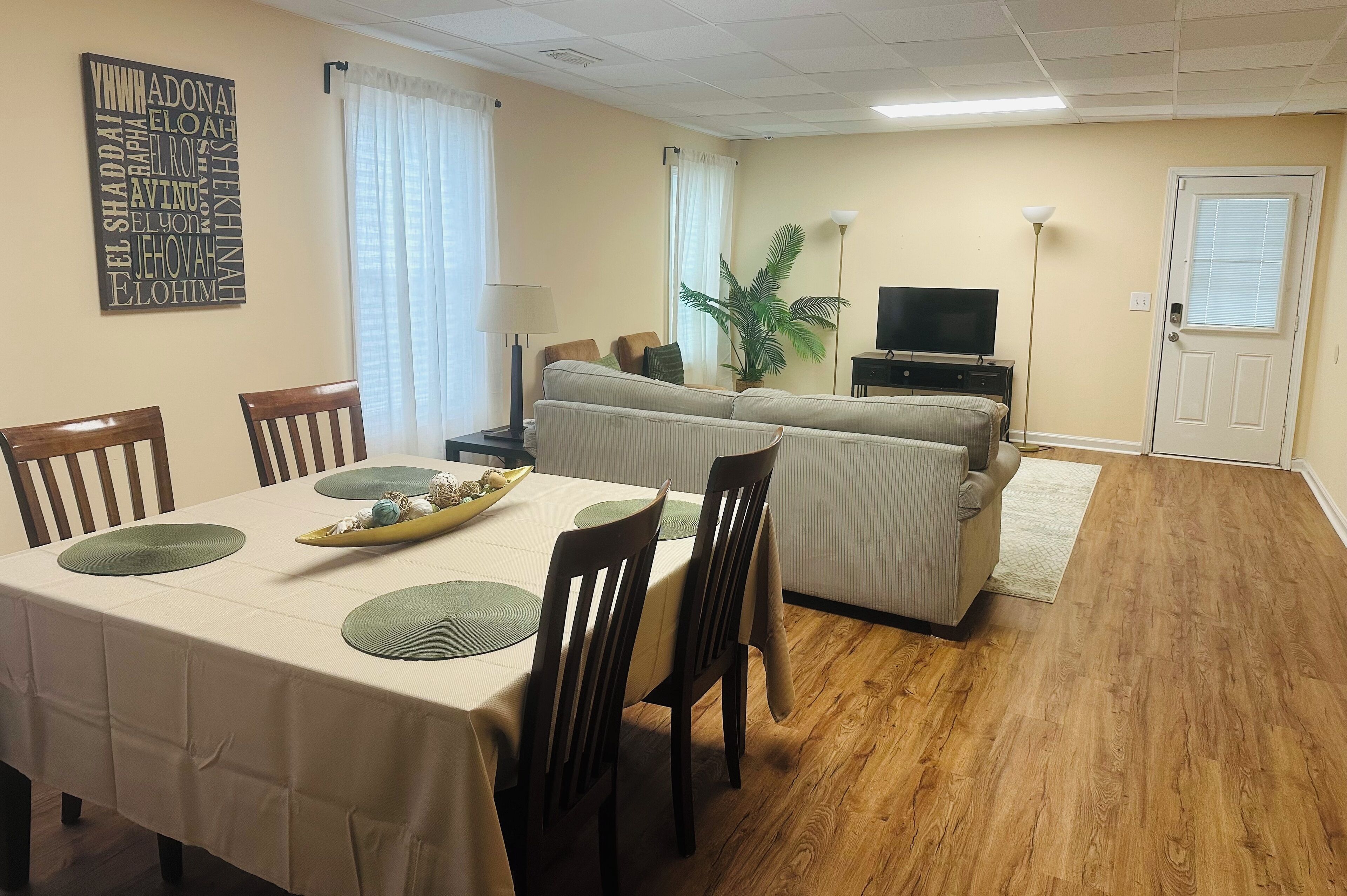 Un coin repas avec une table dressée pour quatre personnes, un canapé, une télévision et une plante.