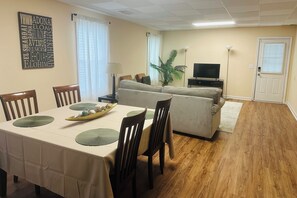 A dining area with a table set for four, a sofa, a television, and a plant.