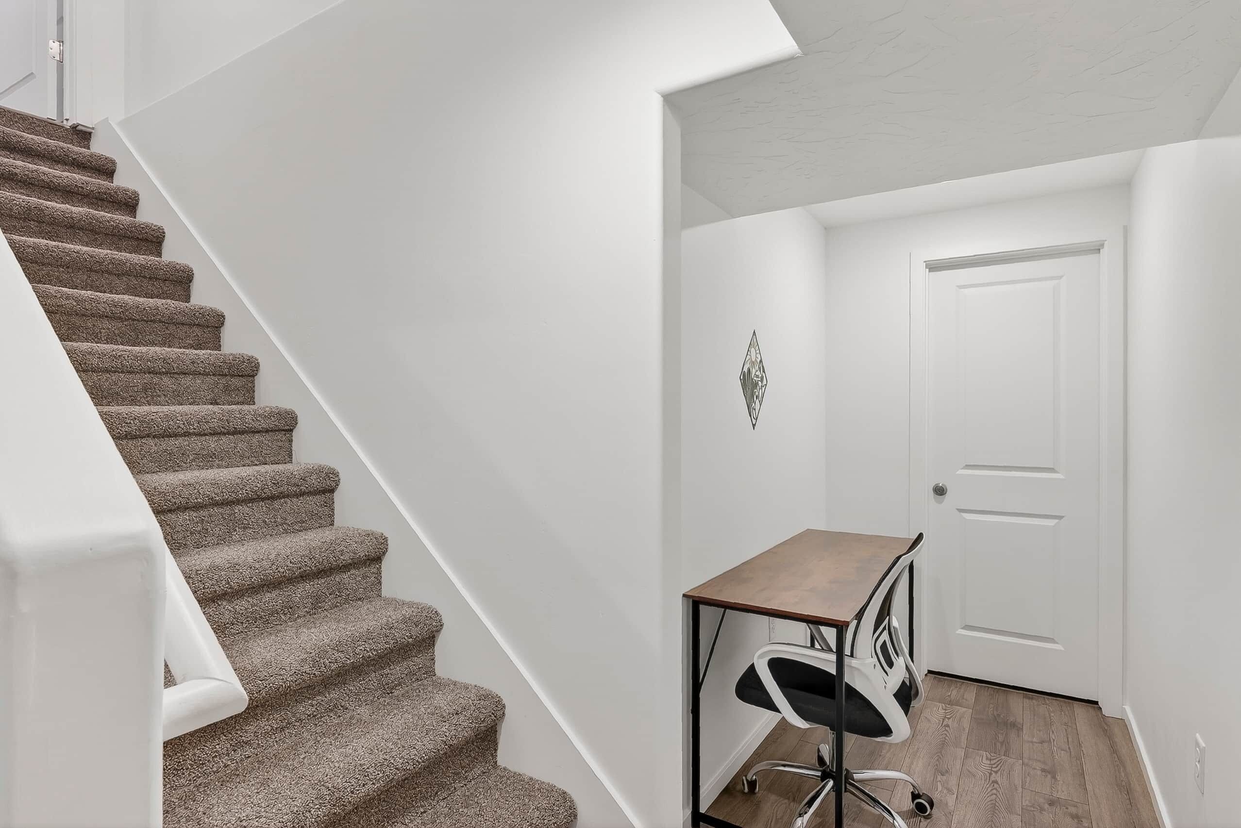 Un escalier avec des marches recouvertes de moquette, une porte blanche et un bureau avec une chaise.