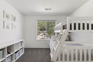 A child's room with bunk beds, a window with a view of trees, and a white ceiling.