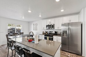 Una cocina moderna con armarios blancos, electrodomésticos de acero inoxidable, una isla central con taburetes y vistas a una pared de piedra.