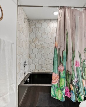 A bathroom with a hexagonal tile wall, a shower curtain with a cactus design, a bathtub, and a towel rack. - Cactus Hideaway Townhome in Cedar City (Cedar City)