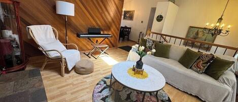 Een gezellige woonkamer met een houten wand, een bank, een fauteuil, een bijzettafeltje en een lamp.