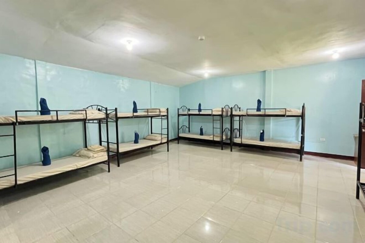 A room with bunk beds arranged in two rows, a tiled floor, and a plain wall.
