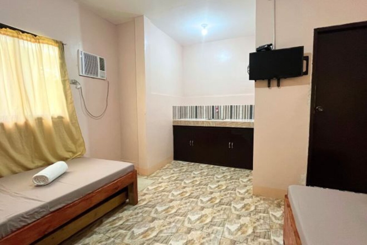 Um quarto pequeno com cama, guarda-roupa, televisão e chuveiro.