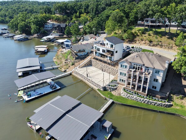 A lakeside property with multiple docks, a large building with balconies, and a well-maintained lawn. - The LOTO Game-Changer: Sand Volleyball Court, No-Wake Cove & a Covered Slip! (Osage Beach)