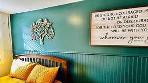 Een slaapkamer met teal muren, een houten bedframe en een gequiltteerde deken in geel. Een motiverende quote staat op de muur.