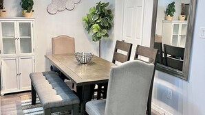 Une salle à manger avec une table en bois, des bancs rembourrés et des chaises. Un grand miroir orne le mur et une plante en pot est posée sur la table.