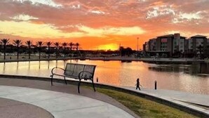 Une vue sur le coucher de soleil au-dessus d’une étendue d’eau, avec un banc et une promenade.