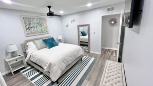 Une chambre à coucher moderne, avec un lit, des tables de chevet, un miroir, un ventilateur de plafond et un téléviseur fixé au mur.
