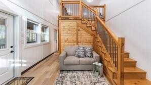 Un escalier avec des rampes en bois menant à un niveau supérieur, un canapé gris avec des coussins à motifs et un tapis à motifs sur le sol.
