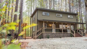Une maison à deux étages avec un porche, entourée d’arbres.