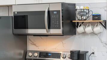 Cocina moderna con electrodomésticos de acero inoxidable, incluyendo un microondas, horno y cafetera.