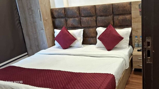 Une chambre d’hôtel avec une tête de lit en bois, un couvre-lit blanc, deux oreillers rouges et une couverture rouge.